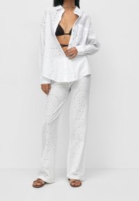 Ensemble chemise et pantalon en tissu œillet blanc avec motif ajouré, découpes détaillées, coupe décontractée, manches longues et silhouette à jambe droite.