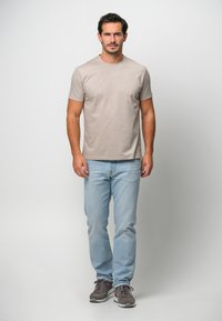 Ljusbeige kortärmad T-shirt med rund halsringning, kombinerad med ljusblå jeans och grå sneakers. Enkel, avslappnad design och passform.