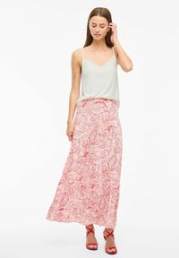 Lange paisley rok in rood en wit, met een vloeiende design en een gelaagde zoom; gecombineerd met een lichte, mouwloze top en rode sandalen.