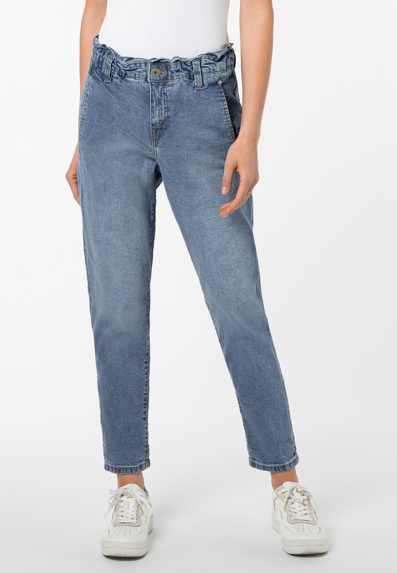 Hellblaue Denim-Jeans mit einem gerafften Bund, der mit einem Knopfverschluss versehen ist, seitlichen Taschen und schmal zulaufenden Beinen, kombiniert mit weißen Sneakers.