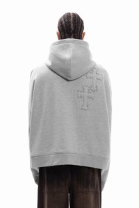 Γκρι φαρδιά μπλούζα με κουκούλα από μαλακό ύφασμα, με κουκούλα και κεντημένα σταυροειδή σχέδια στην πλάτη. Συνδυασμένη με σκούρο καφέ παντελόνι.