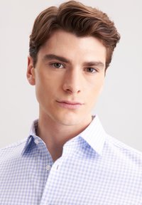 Camicia a quadri blu chiaro e bianca con colletto, dotata di chiusura con bottoni sul davanti e una texture liscia, indossata da un modello con capelli corti.