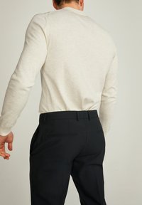 Hellgraues Langarmshirt aus weichem Material, kombiniert mit maßgeschneiderten schwarzen Hosen mit Seitentaschen und glatter Oberfläche.