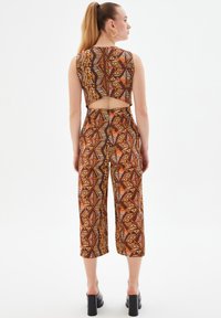 Conjunto de dos piezas con estampado en marrón, naranja y crema. Presenta una blusa corta con corte en la espalda y pantalones anchos hasta los tobillos.