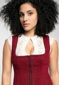 Rotes Reißverschlusskleid mit kunstvoller Spitzenverzierung am Ausschnitt, kombiniert mit einer weißen Spitzenbluse mit fransigen Ärmelenden.