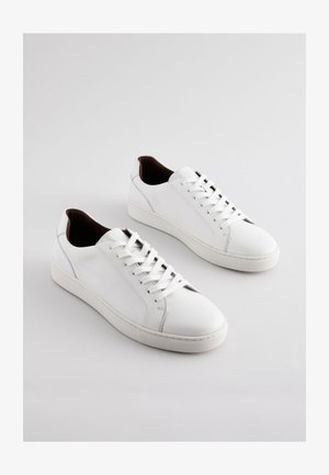 Pantofi sport din piele albă, cu profil jos, părți laterale perforate, șireturi plate și captuseală interioară maro contrastantă. Talpă din cauciuc cu model texturat.