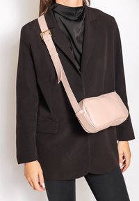 Piccola borsa a tracolla in pelle rosa, con forma rettangolare e superficie liscia, dotata di una lunga tracolla regolabile e una chiusura a zip discreta.