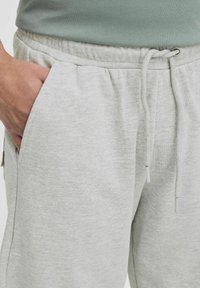Un pantalon de survêtement gris clair avec une taille à cordon, des poches latérales et un tissu doux et texturé. Idéal pour une tenue décontractée et confortable.
