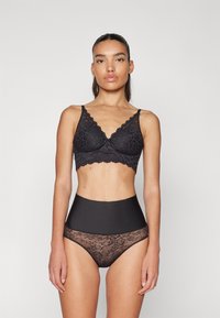 Svart spets-bandeau behå med blommönster och vågiga kanter, i kombination med höga svarta trosor med genomskinliga spetspaneler.