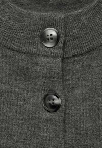 Grijze gebreide cardigan met een ribgebreide kraag en twee ronde zwarte knopen aan de voorkant. De textuur lijkt zacht en glad te zijn.
