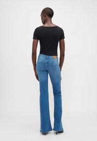 Blå utsvängda jeans med ljus tvätt, stickade bakfickor och en beige läderpatch vid midjan. Matchat med en åtsittande svart t-shirt.