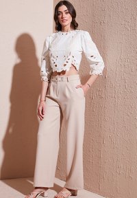 White cropped blouse with floral cutouts, paired with beige wide-leg trousers featuring front buttons and pockets. Clear texture, loose fit.