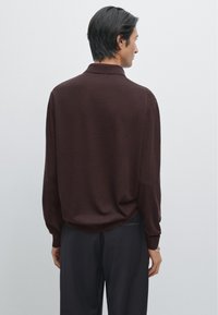 Donkerbruine poloshirt met lange mouwen van een zachte stof, met een opgerolde kraag en een relaxte pasvorm, gecombineerd met donkere broeken.