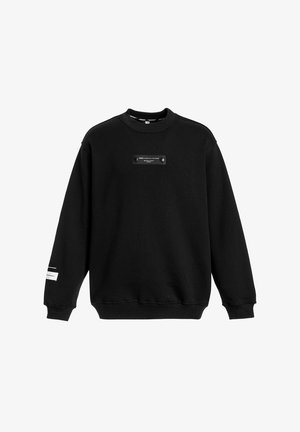 Sudadera negra con cuello redondo, mangas largas y un parche con logo en la parte delantera que presenta dos acentos circulares. Tejido suave con un ajuste casual.