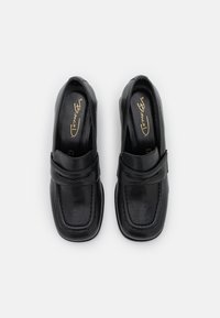 Sorte læder loafers med syninger, rundet tå og en rem tværs over fronten. Glat tekstur med subtil glans.