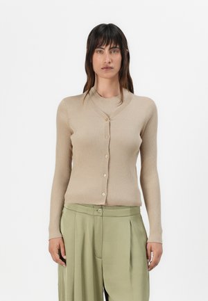 Cardigan beige côtelé avec un décolleté en V et une fermeture à boutons, doté de manches longues et d'une coupe ajustée. Assorti à un pantalon plissé vert clair.