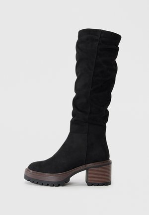 Bottes noires en suède, à hauteur de genou, avec un design drapé, un bout rond et un solide talon en bloc marron avec une surface texturée.