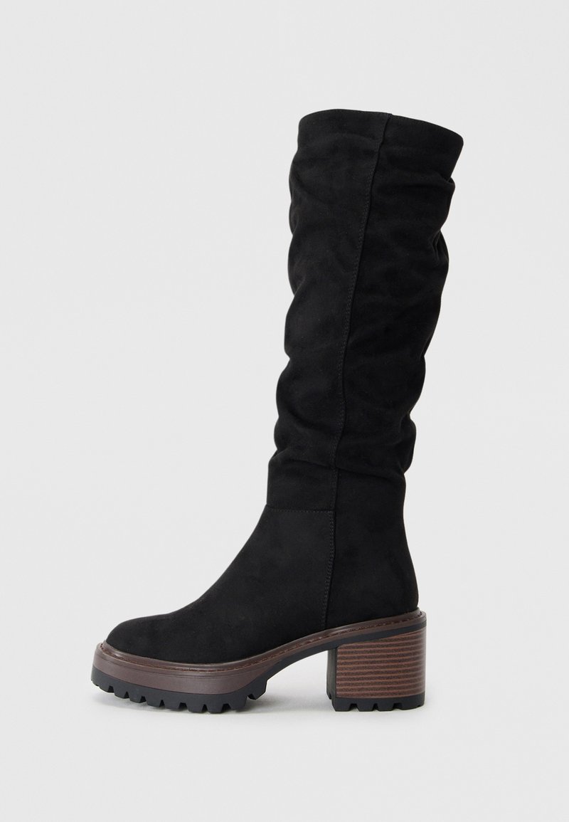 Bottes noires en suède, à hauteur de genou, avec un design drapé, un bout rond et un solide talon en bloc marron avec une surface texturée.