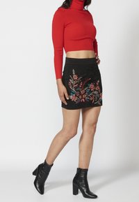 Gonna nera con ricami floreali in rosso, blu e verde. Abbinata a un dolcevita rosso aderente e stivaletti neri con tacco.