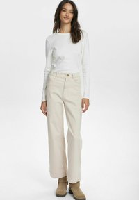 Off-white långärmad topp som matchas med ljusbeige vida jeans, med knäppning och uppvikta ärmslut. Suede ankelstövlar fulländar looken.