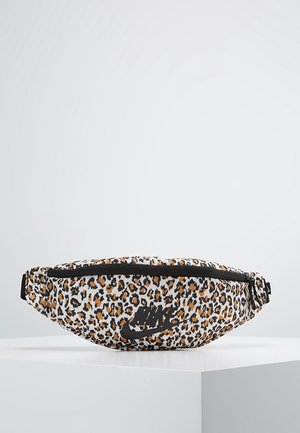 Sac banane imprimé léopard avec fermeture éclair noire et logo Nike noir posé sur un socle blanc sur fond gris uni.