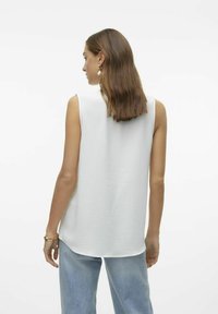 Débardeur blanc sans manches en tissu texturé, col rond et coupe décontractée, associé à un jean en denim bleu clair.
