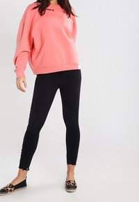 Sudadera rosa de gran tamaño con texto negro, combinada con jeans ajustados negros con dobladillo desflecado y espadrilles de print de leopardo.