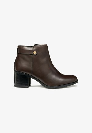 Bottines en cuir marron avec un bout rond, fermeture éclair et un petit talon carré. Elles présentent une sangle avec un détail de bouton doré.