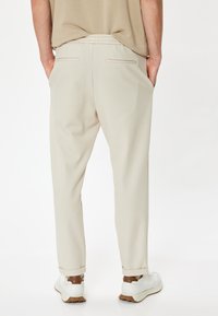 Pantalones beige con un corte ajustado y cinturilla elástica, que presentan dos bolsillos traseros y detalles de costura sutiles. Combinados con zapatillas blancas.