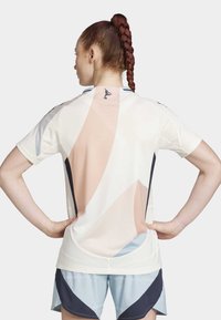 Jersey deportivo de color claro con grandes patrones geométricos en suave rosa, azul y crema. Presenta un cuello redondo y mangas cortas.