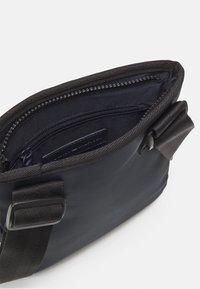 Schwarze Nylon-Tasche mit einem Reißverschlussoberteil, ausgestattet mit einem glatten Innenfutter und einer zusätzlichen Reißverschlusstasche. Robuste Träger und elegantes Design.