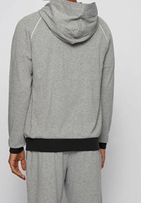 Sudadera con capucha gris hecha de tela suave, con capucha, ribete negro en el dobladillo y los puños, y sutiles detalles blancos a lo largo de las costuras.