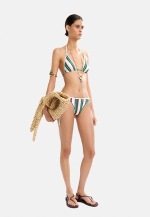 Paskowany bikini w kolorze zielonym, białym i różowym. Modelka trzyma plecioną torbę ze słomy. Dodatki to złota opaska na ramię i naszyjnik z koralików.