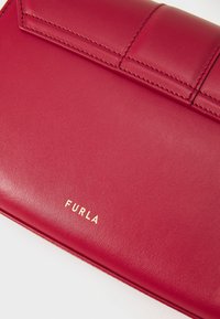 Clutch in pelle rossa con una texture liscia, caratterizzato dal logo dorato "FURLA" e da accenti cuciti sul bavero. Design compatto e rettangolare.