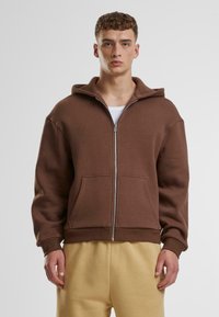 Brauner Zip-Hoodie mit Kapuze, Fronttaschen und lässiger Passform. Hergestellt aus weichem Stoff, mit gerippten Bündchen und Saum.