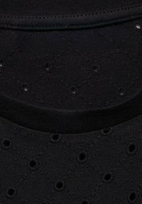 Black textured fabric featuring a floral pattern with perforations, rounded neckline, and a smooth ribbed hem.
