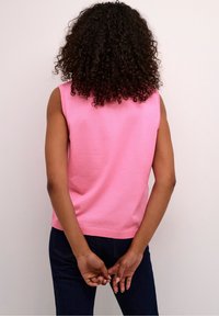 Beżowy top bez rękawów wykonany z dzianiny, z okrągłym dekoltem, prążkowanym dołem i gładką fakturą, w połączeniu z ciemnymi dżinsami.