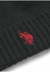 Crni pleteni beanie sa rebrastom teksturom, koji se ističe velikim crvenim izvezenim logom sprijeda. Izdržljiv materijal od mješavine vune.