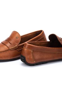 Mocasines de cuero marrón con un diseño clásico. Presentan detalles de costura y una correa decorativa; suela de goma para tracción y durabilidad.