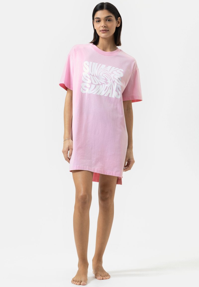 Robe t-shirt en coton rose avec un design de texte en spirale blanc qui dit "DIMANCHES". Manches courtes, coupe décontractée et ourlet au niveau des genoux.