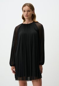 Zwarte geplooide jurk met een ronde hals, transparante lange mouwen en een vloeiende silhouet. Gemaakt van een lichtgewicht stof met een gladde textuur.