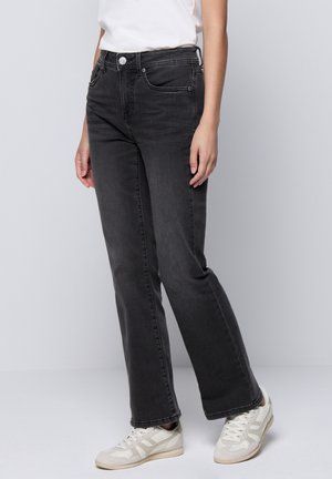 Slim-fit zwarte denim jeans met een middelhoge taille, met voorzakken en een knoopsluiting. Gecombineerd met lichtgekleurde sneakers.