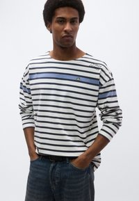 Ριγέ πουκάμισο με μακριά μανίκια σε λευκό, ναυτικό μπλε και ανοιχτό μπλε. Διαθέτει στρογγυλή λαιμόκοψη, άνετη εφαρμογή και κεντημένα διακοσμητικά στο στήθος και τα μα νίκια.