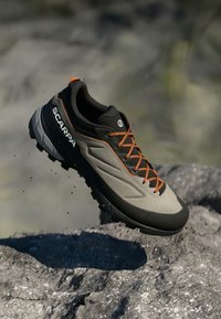 Graue und schwarze Trail-Laufschuhe mit orangen Schnürsenkeln, ausgestattet mit einem strukturierten Obermaterial, einer robusten Sohle und einem Logo an der Seite, entworfen für den Einsatz im Freien.