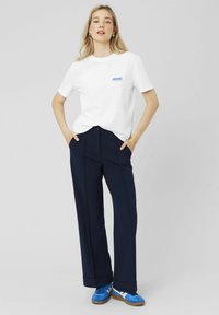T-shirt en coton blanc avec "MORE" imprimé en bleu, associé à un pantalon large bleu marine et des baskets bleues. Tenue simple et décontractée.