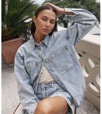 Hele sinine denim jakk koos kulumistega, kaks esimest taskut, nööpidega kinnitamine, kantud beeži topi ja denim lühikeste püksidega.