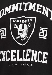 Schwarzes Baumwoll-T-Shirt mit weißen Grafiken. Die Vorderseite zeigt "VERPFLICHTUNG" und "EXZELLENZ" sowie das Raiders-Logo und das "20"-Emblem.