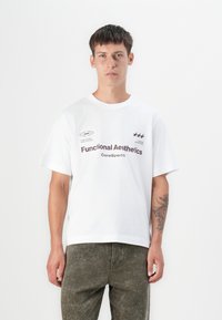 White cotton t-shirt with short sleeves, crew neck, and printed black text, worn with textured olive green pants.