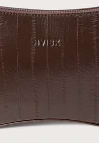 Bolso de mano de cuero marrón con forma curva, branding en relieve y superficie texturizada con patrones de líneas verticales. Cierre con cremallera en la parte superior.