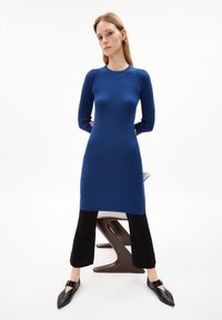 Gestreiftes blaues Strickkleid mit langen Ärmeln, Rundhalsausschnitt und geradem Schnitt. Kombiniert mit schwarzen cropped Hosen und spitzen schwarzen Ballerinas.